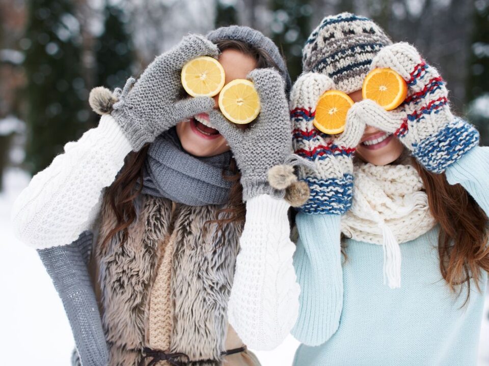 Dwie dziewczyny w zimowych czapkach trzymające pomarańcze na oczach.